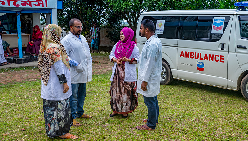 Healthcare professionals standing outdoors, having a conversation in front of an ambulance