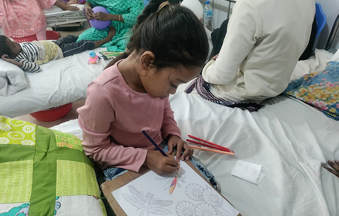 Adiba Amin Maria on a hospital bed, drawing flowers on a piece of paper.
